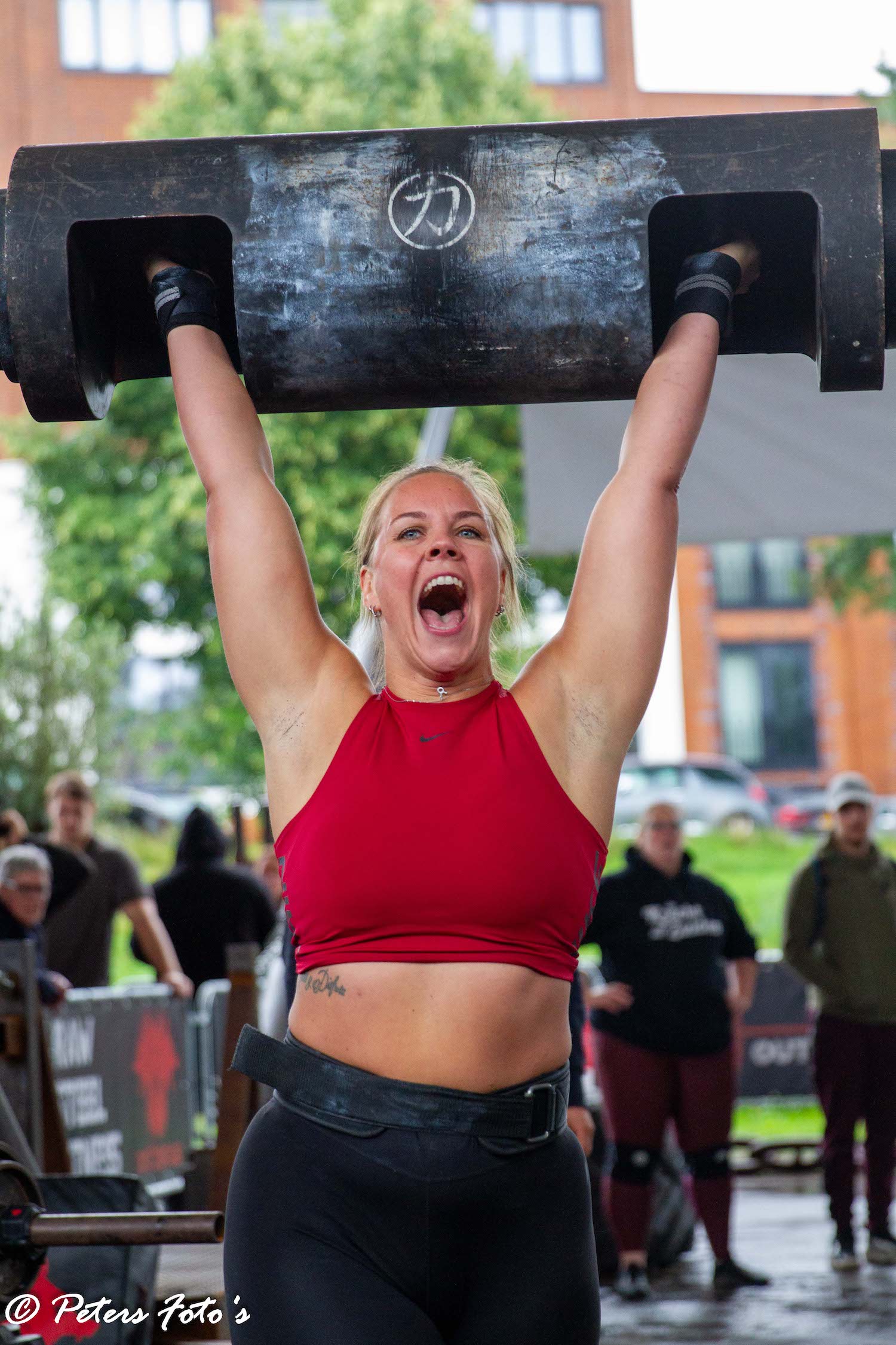 An athlete in a red top celebrating with a log locked out overhead.