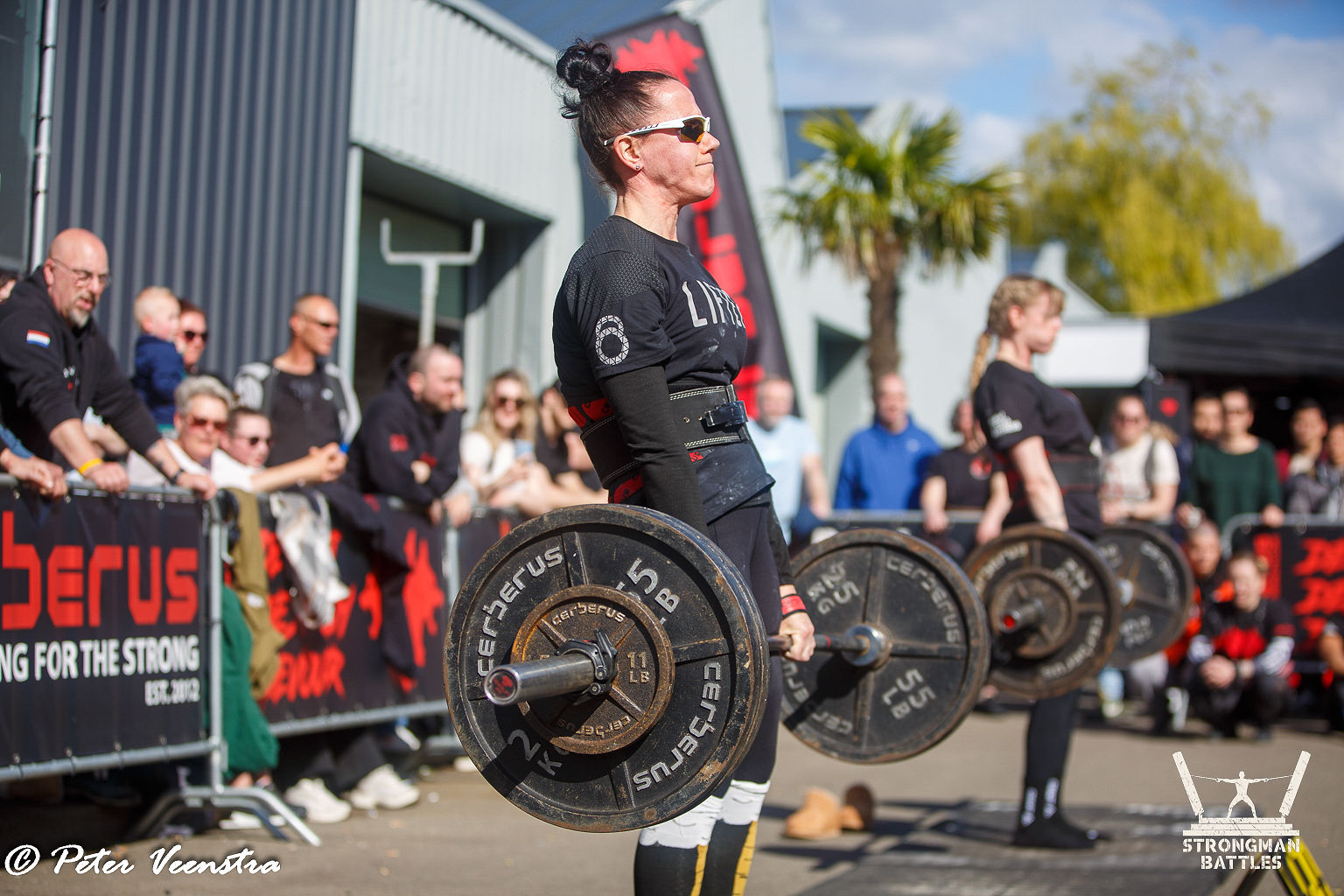 A woman performing a deadlift in front of spectators at a 2025 natural strongwoman competition.