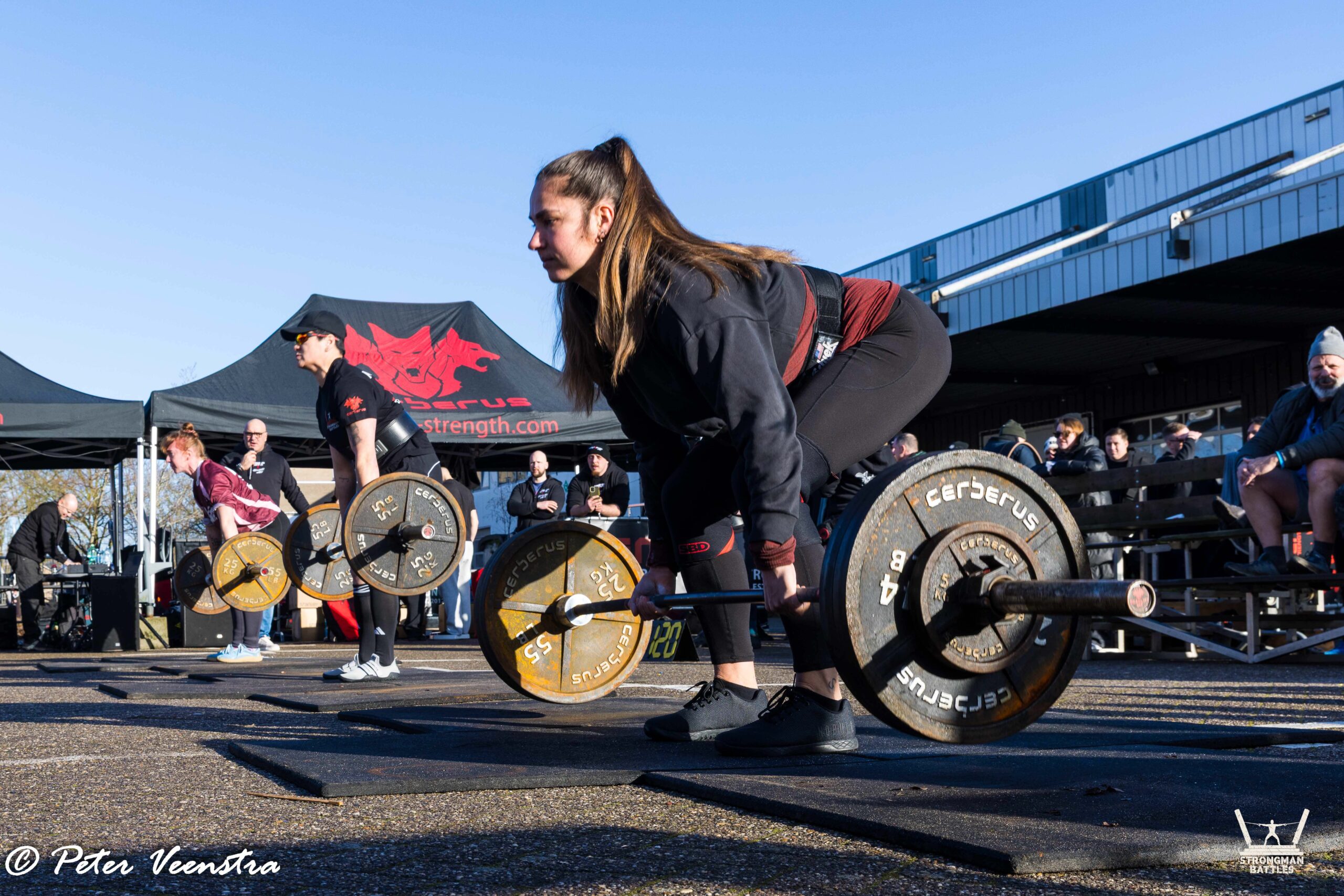 Three women competing in the deadlift at Strongman Battles Eindhoven, with spectators behind them