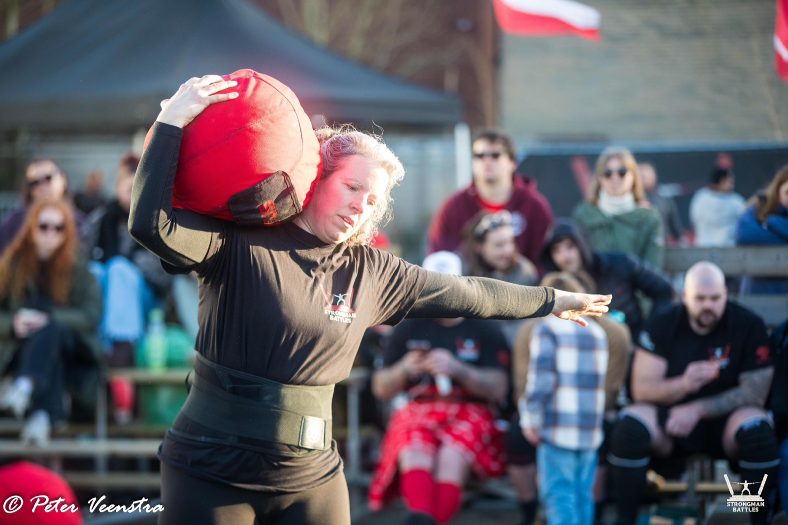 A Strongman Battles athlete lifting a sandbag in front of supporters in Eindhoven.